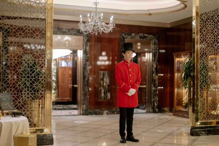 Uniformed doorman standing in an elegant hotel lobby, ready to welcome guests with discreet luxury service.