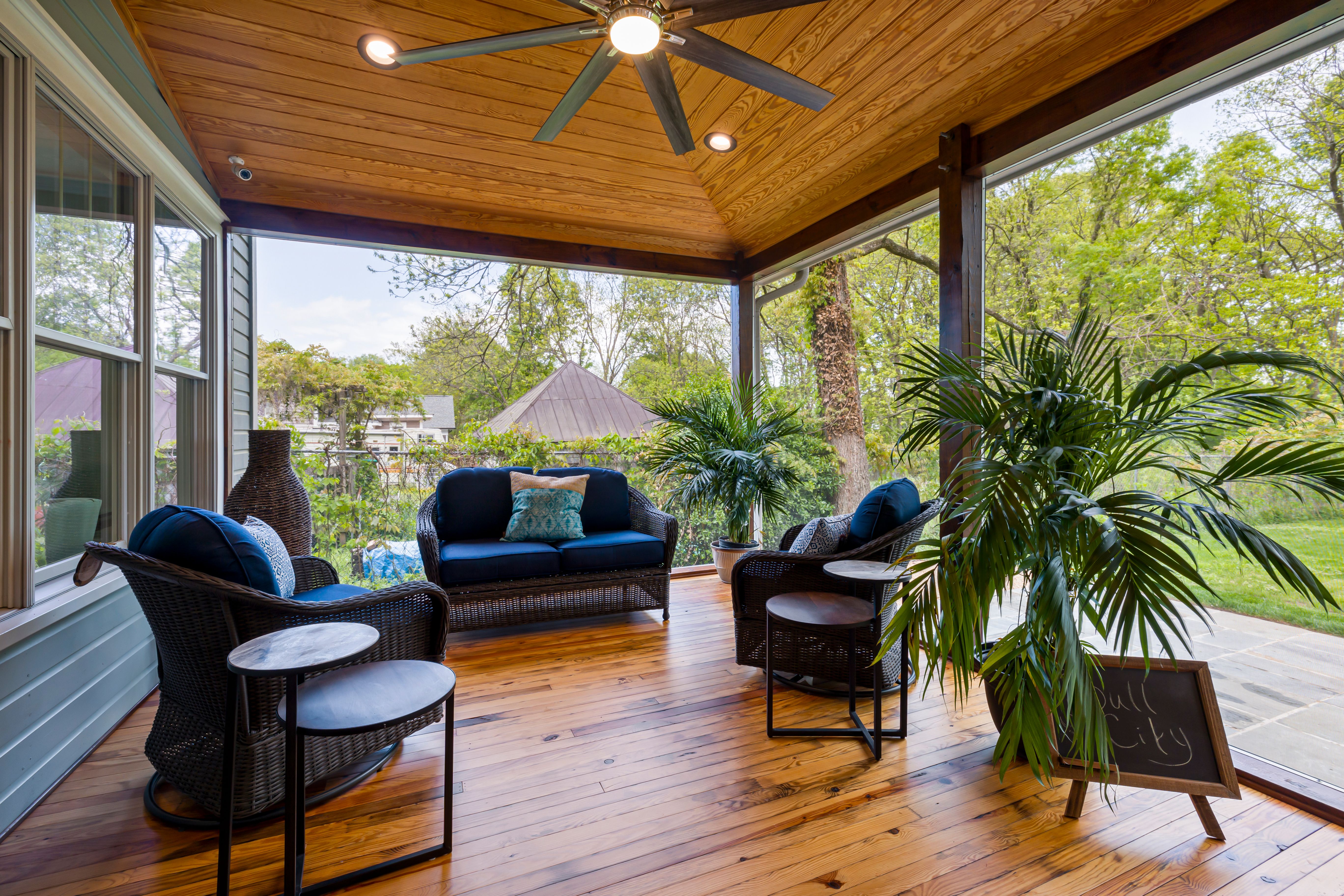 Modern outdoor patio with cushioned seating, warm wood flooring, and lush greenery.