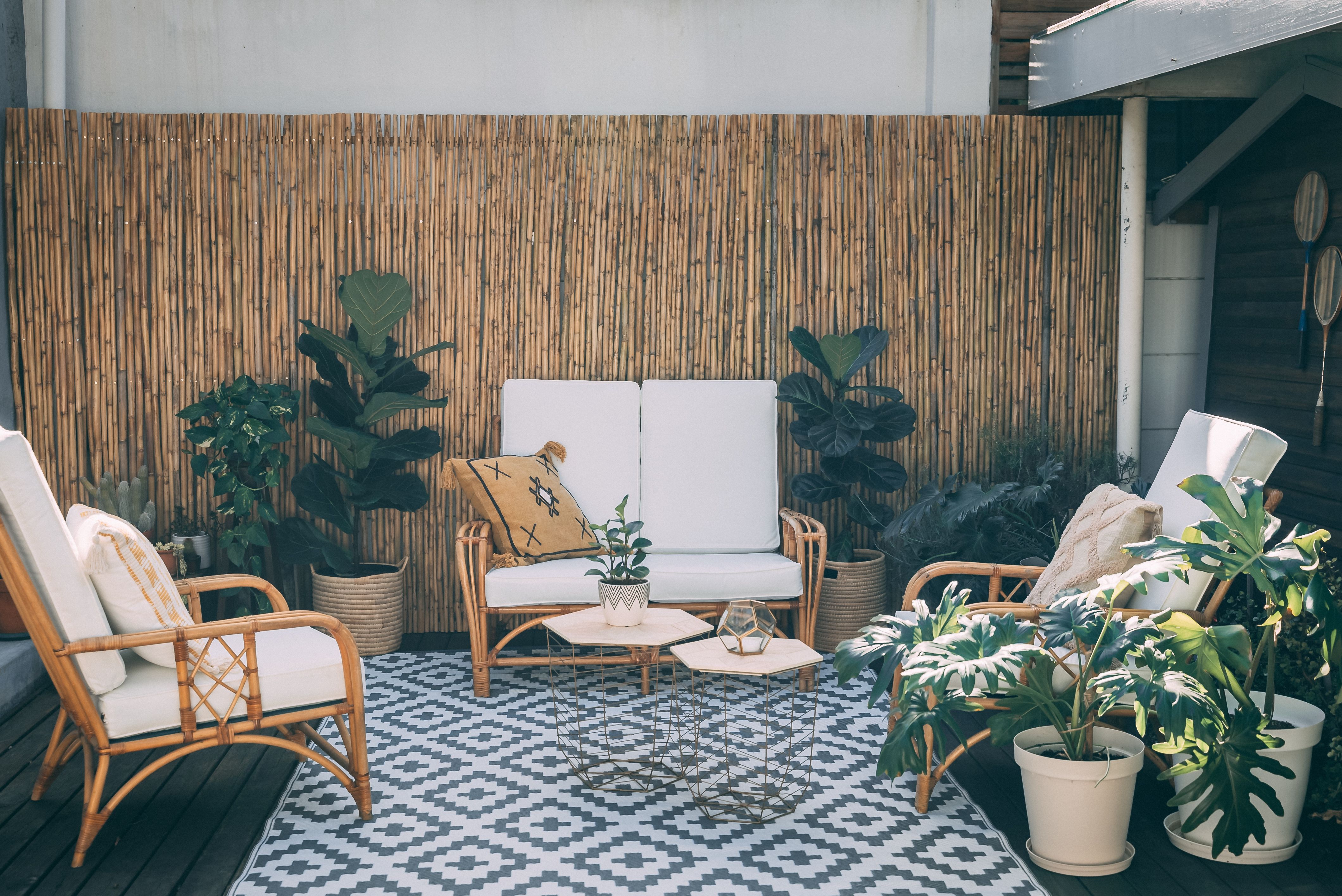 Rattan patio furniture, potted plants, and natural bamboo details create a serene outdoor living space.