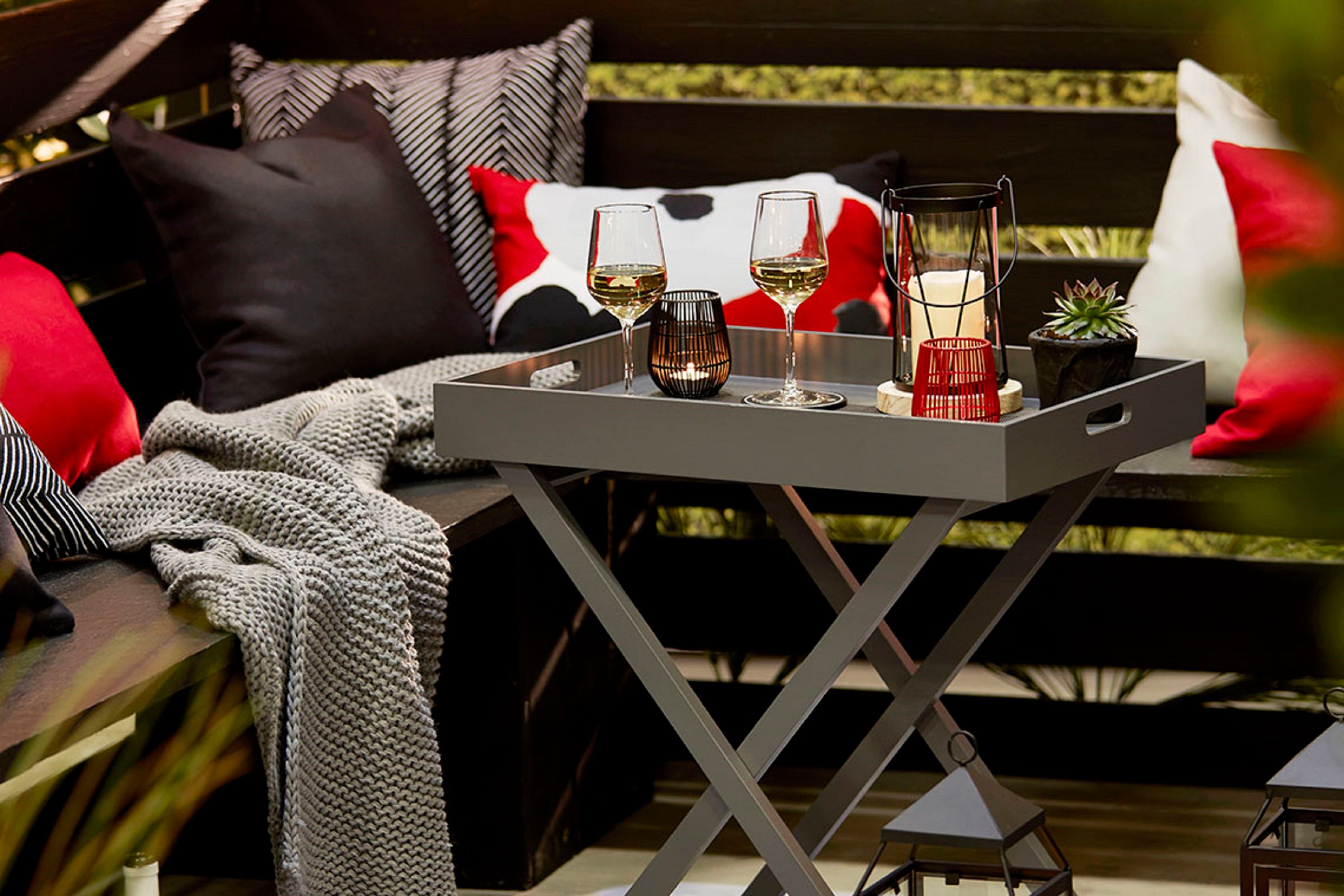 An elegant outdoor lounge arranged with cushions, wine glasses, and candles for stylish entertaining.